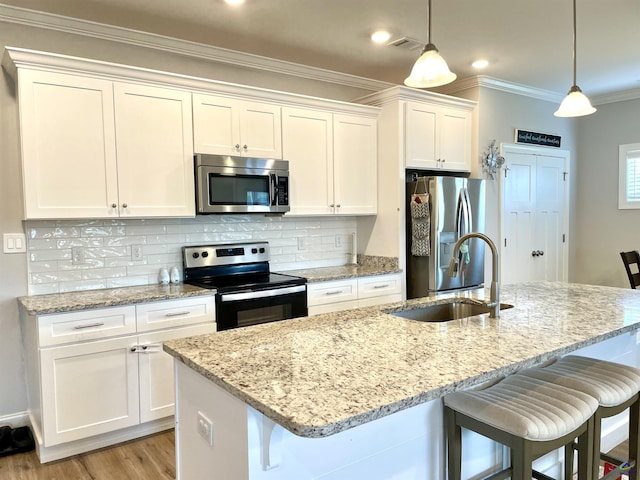 kitchen featuring appliances with stainless steel finishes, a sink, crown molding, white cabinetry, and a kitchen island with sink