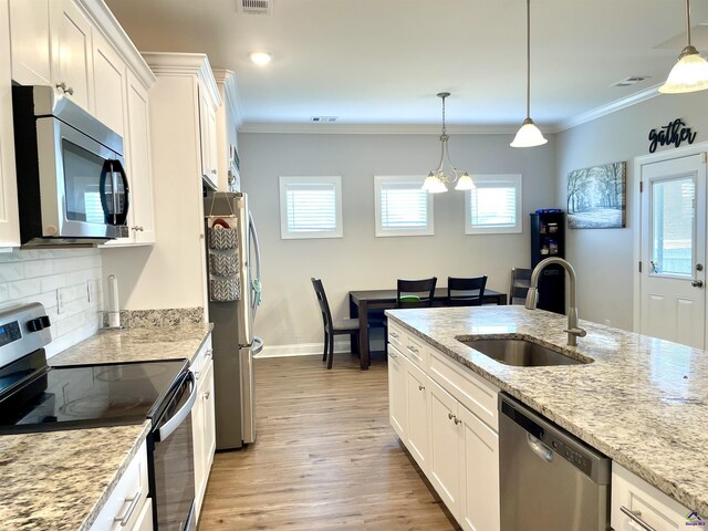 kitchen with appliances with stainless steel finishes, a sink, light wood-style flooring, white cabinetry, and ornamental molding