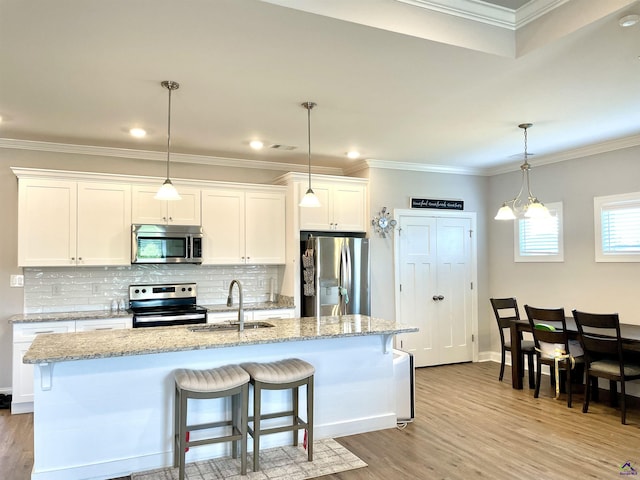 kitchen featuring appliances with stainless steel finishes, light wood finished floors, a sink, white cabinets, and ornamental molding