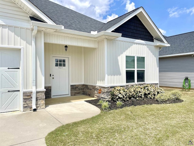 entrance to property with stone siding, a shingled roof, and a yard