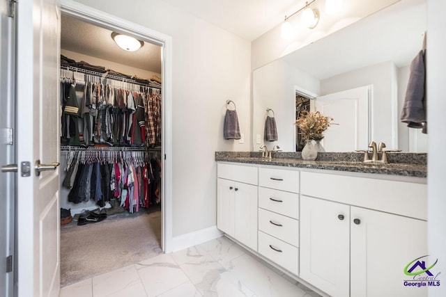bathroom with double vanity, marble finish floors, a walk in closet, and baseboards