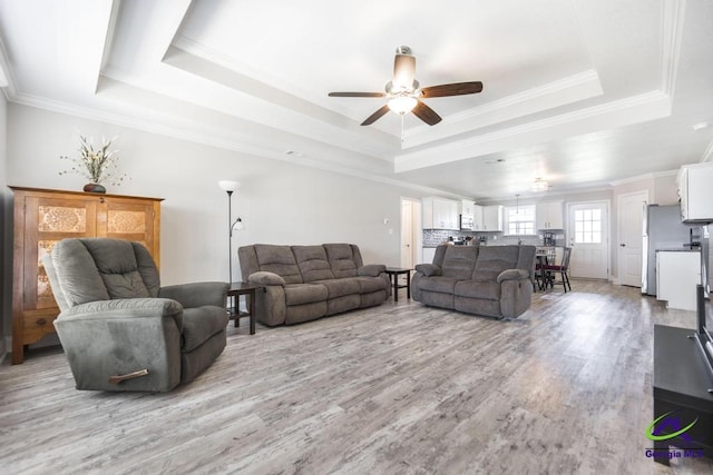 living area with a raised ceiling, a ceiling fan, light wood finished floors, and ornamental molding