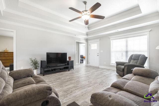 living area featuring a raised ceiling, a ceiling fan, crown molding, wood finished floors, and baseboards