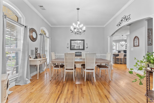 dining area with a chandelier, light wood-style floors, decorative columns, crown molding, and arched walkways