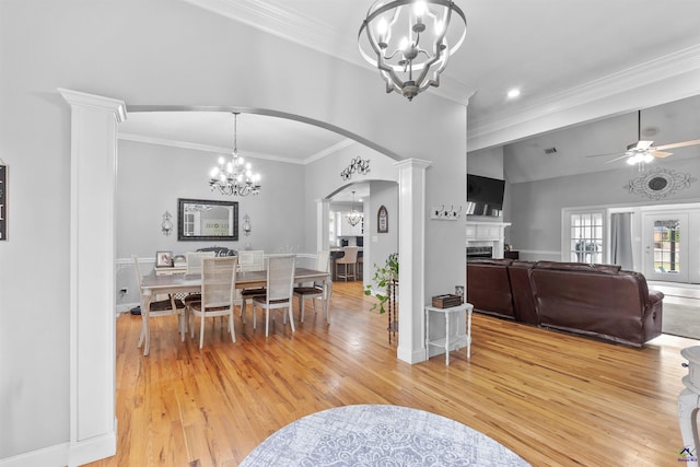 dining space featuring light wood-type flooring, a chandelier, a fireplace, arched walkways, and crown molding