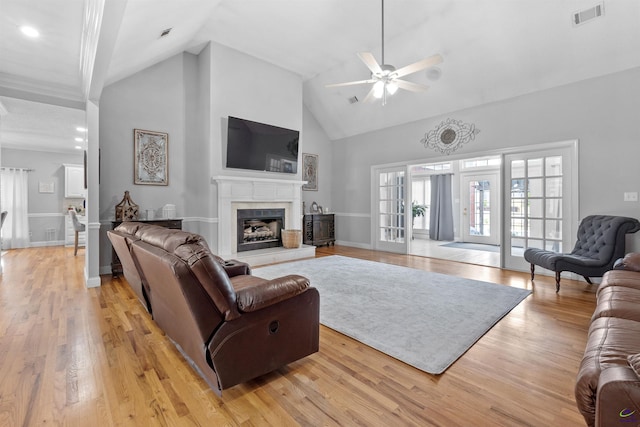 living room with ceiling fan, high vaulted ceiling, light wood finished floors, a tile fireplace, and baseboards