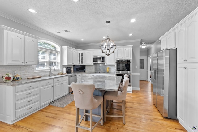 kitchen featuring stainless steel appliances, white cabinetry, a center island, a sink, and light wood-style flooring