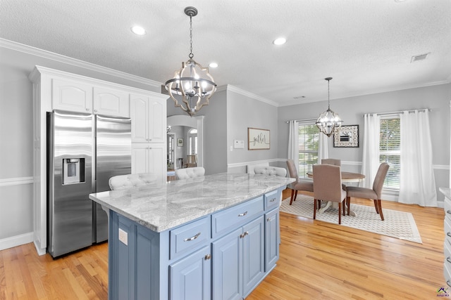 kitchen with stainless steel fridge, a chandelier, a textured ceiling, arched walkways, and white cabinetry