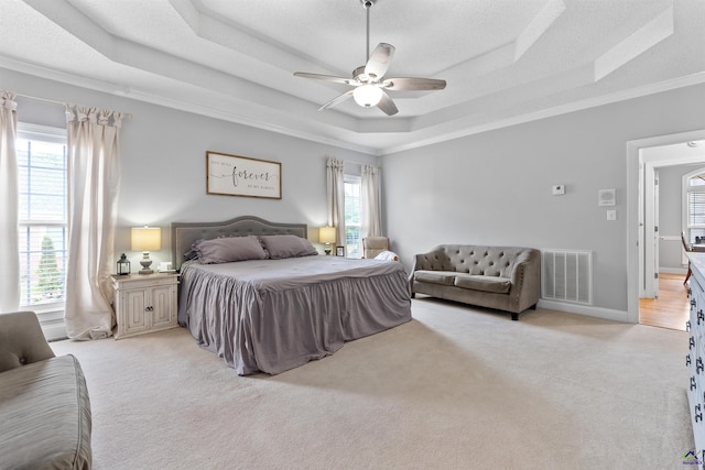 bedroom featuring a raised ceiling, light colored carpet, ornamental molding, and a ceiling fan