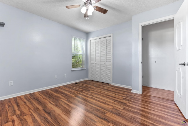unfurnished bedroom with dark wood-style flooring, a textured ceiling, a closet, baseboards, and a ceiling fan