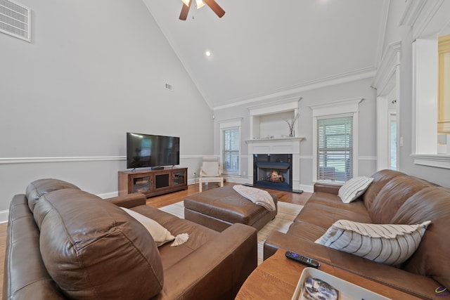 living room with ceiling fan, wood finished floors, high vaulted ceiling, a lit fireplace, and healthy amount of natural light