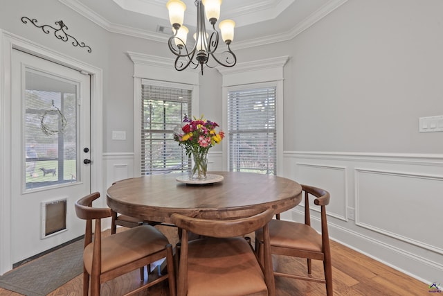 dining area with a chandelier, light wood-style flooring, crown molding, a decorative wall, and a wainscoted wall