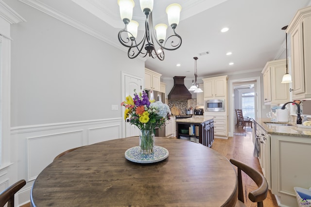 dining area featuring a chandelier, crown molding, light wood finished floors, recessed lighting, and wainscoting