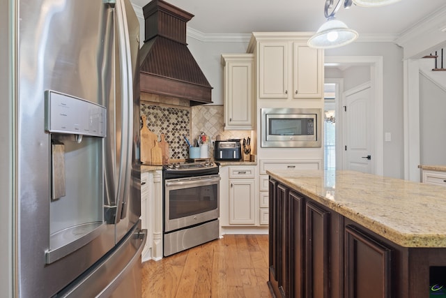 kitchen featuring stainless steel appliances, premium range hood, crown molding, light wood-style floors, and backsplash