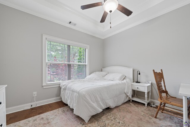 bedroom featuring wood finished floors, ornamental molding, a raised ceiling, baseboards, and a ceiling fan