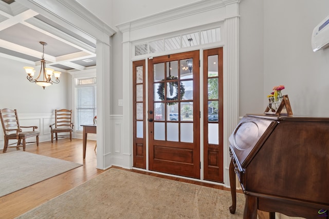 foyer with coffered ceiling, a chandelier, wood finished floors, a wall unit AC, and ornamental molding