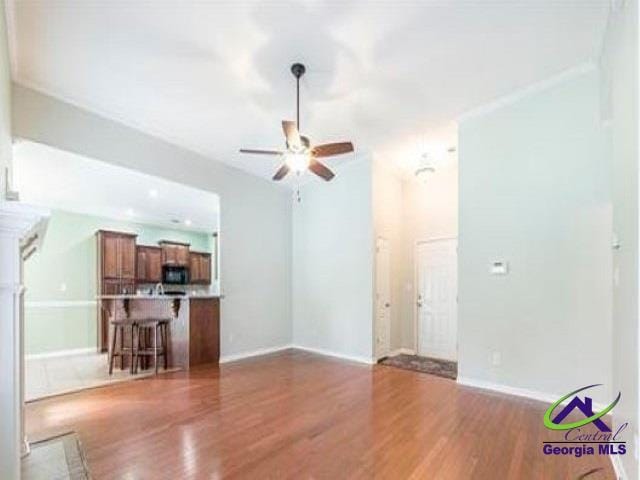 unfurnished living room featuring a ceiling fan, wood finished floors, and baseboards