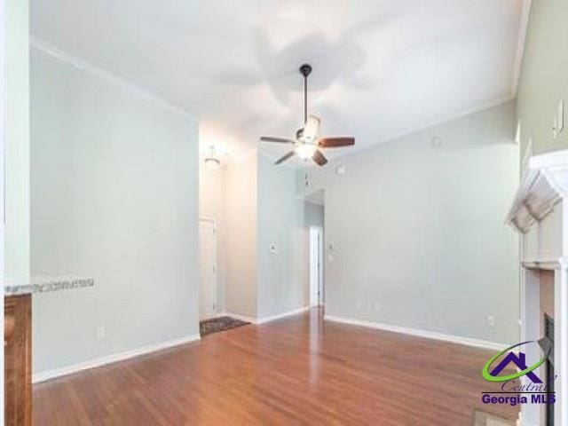 unfurnished living room featuring a ceiling fan, wood finished floors, baseboards, and ornamental molding