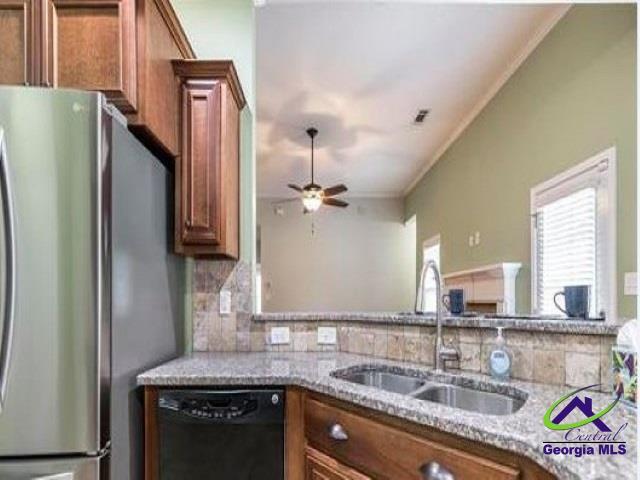 kitchen featuring freestanding refrigerator, dishwasher, a sink, brown cabinetry, and tasteful backsplash