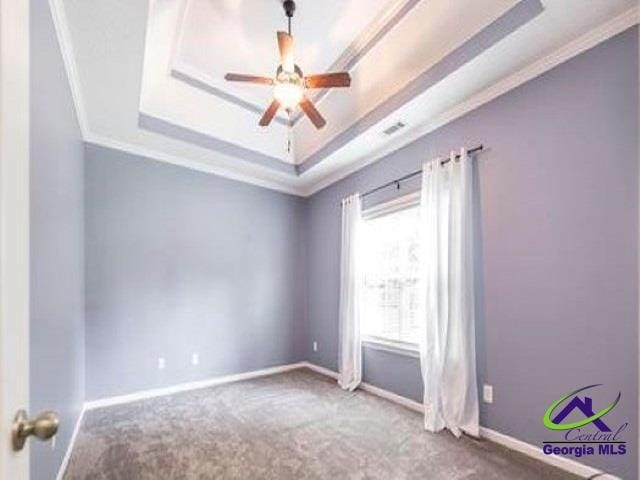 unfurnished room featuring a tray ceiling, ornamental molding, carpet flooring, a ceiling fan, and baseboards