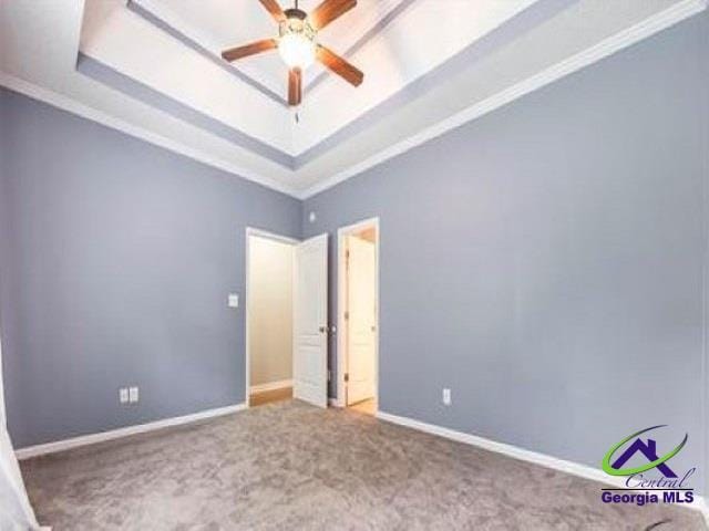 unfurnished bedroom with a tray ceiling, carpet, ornamental molding, and baseboards