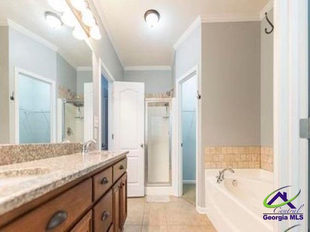 bathroom featuring a shower stall, tile patterned flooring, crown molding, a bath, and double vanity