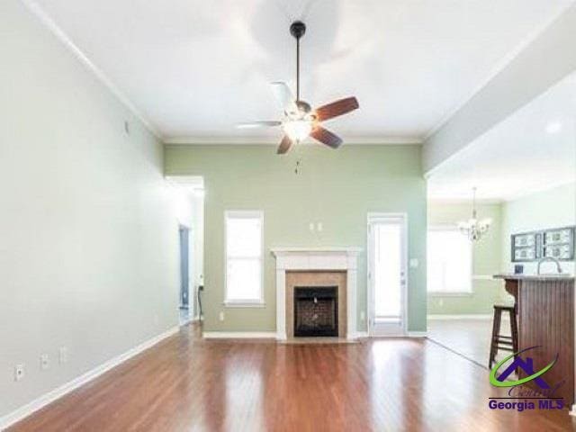 unfurnished living room featuring baseboards, wood finished floors, ceiling fan, a fireplace with flush hearth, and crown molding