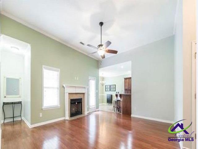 unfurnished living room featuring a ceiling fan, wood finished floors, a fireplace with flush hearth, baseboards, and ornamental molding