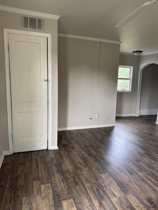 unfurnished room featuring arched walkways, crown molding, dark wood finished floors, and baseboards