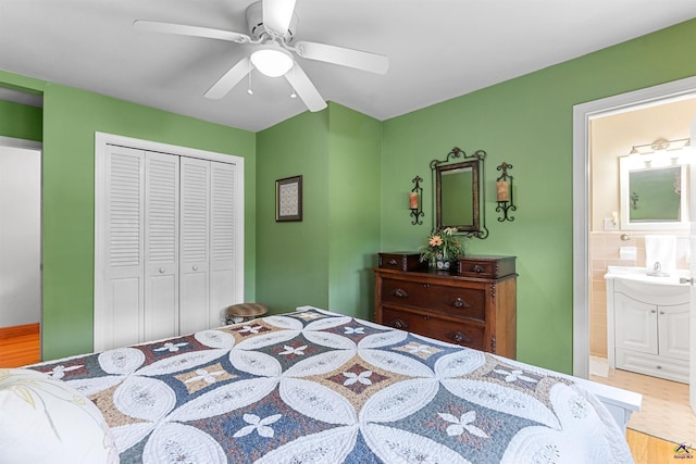 bedroom featuring wood finished floors, a closet, ensuite bath, ceiling fan, and a sink