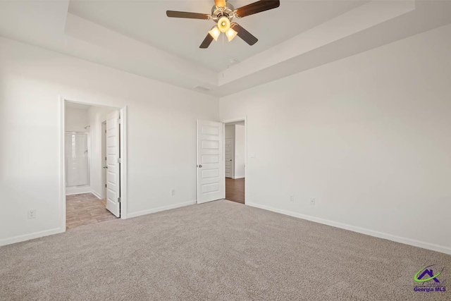 unfurnished bedroom featuring carpet flooring, a tray ceiling, baseboards, connected bathroom, and ceiling fan