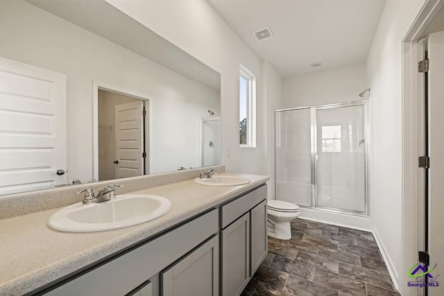 full bathroom featuring a stall shower, stone finish flooring, toilet, double vanity, and baseboards
