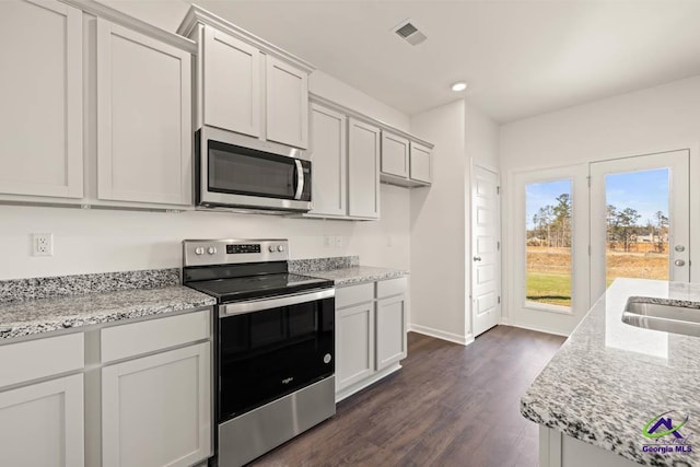 kitchen featuring stainless steel appliances, dark wood finished floors, light stone counters, baseboards, and a sink