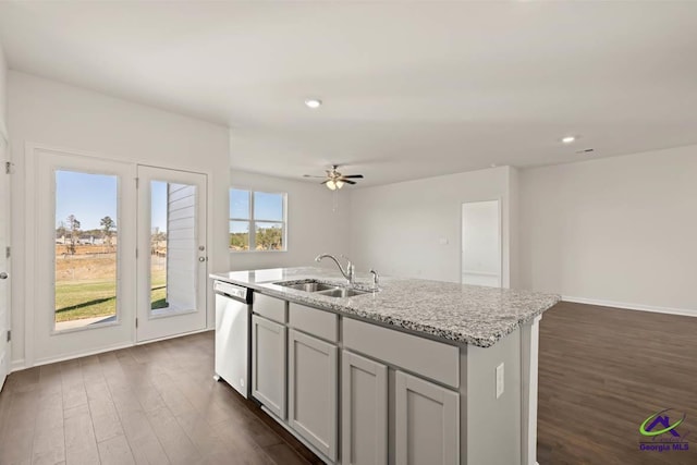 kitchen featuring a sink, dishwasher, dark wood-type flooring, a kitchen island with sink, and light stone countertops