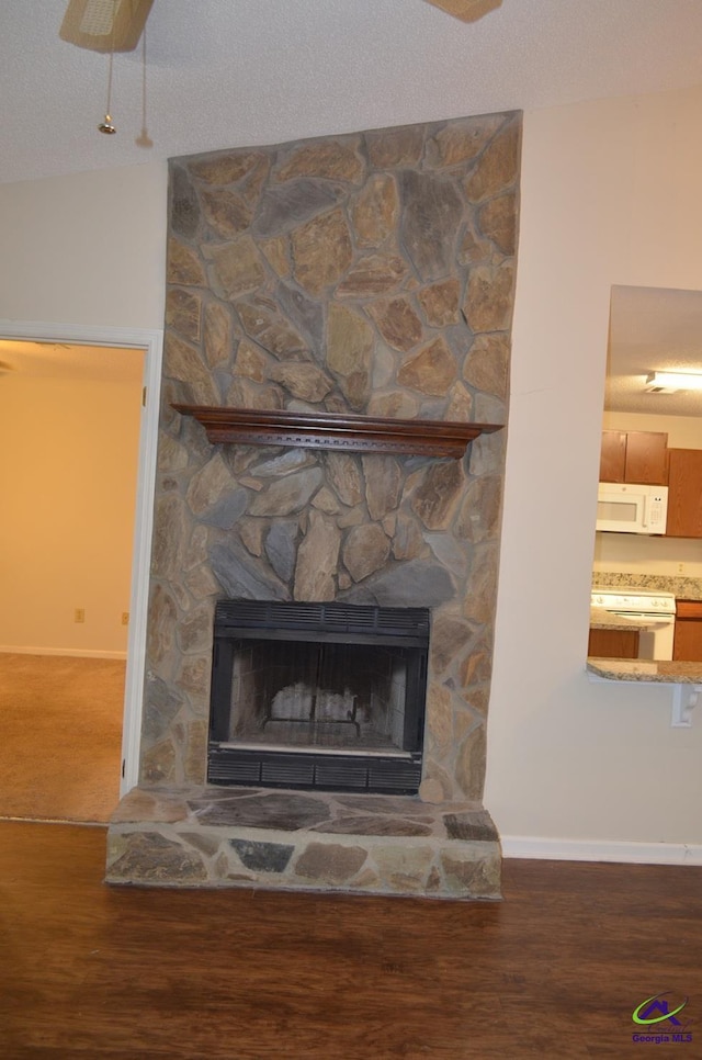 detailed view of white appliances, wood finished floors, a stone fireplace, and baseboards