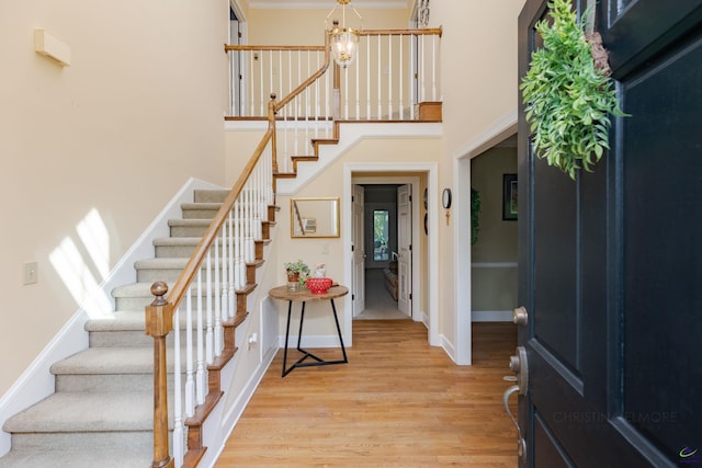 foyer entrance with stairs, light wood-style floors, a chandelier, baseboards, and a high ceiling