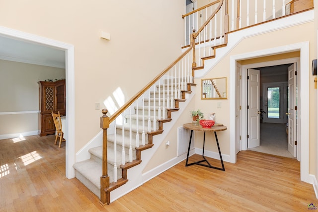 stairway with wood finished floors, baseboards, and crown molding