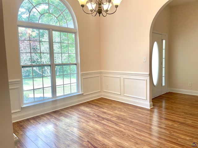 1187 Camden Ct, Warner Robins, GA 31088 - empty room featuring healthy amount of natural light, a chandelier, wood finished floors, arched walkways, and wainscoting