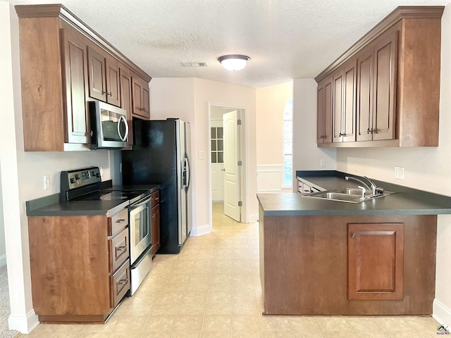 1187 Camden Ct, Warner Robins, GA 31088 - kitchen featuring stainless steel appliances, a sink, dark countertops, a textured ceiling, and a peninsula