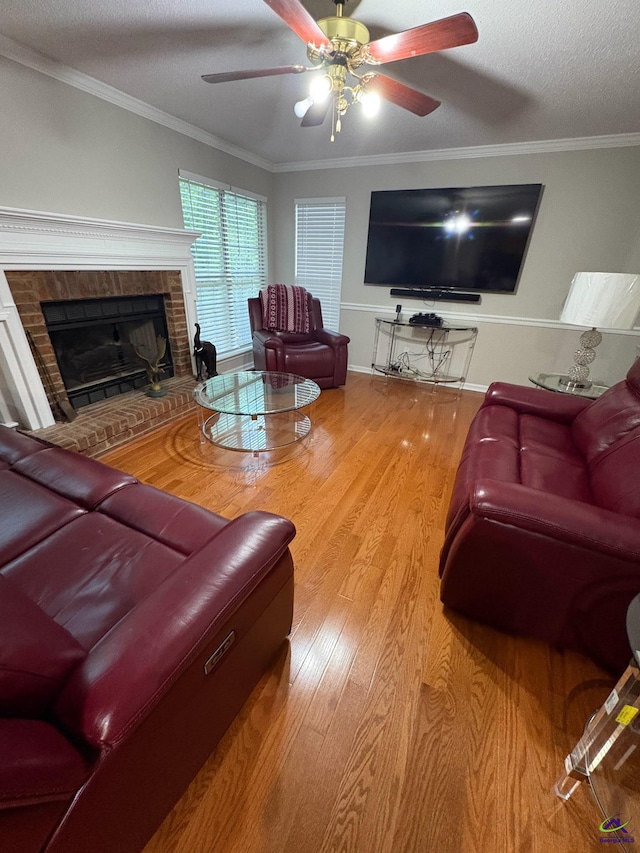 living area featuring wood finished floors, a ceiling fan, a brick fireplace, crown molding, and a textured ceiling