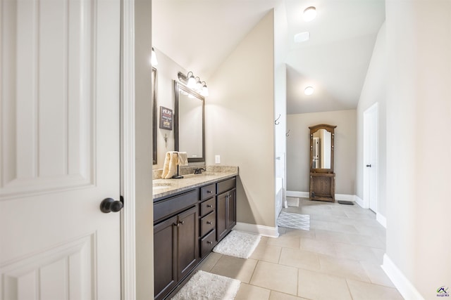 full bath with lofted ceiling, tile patterned floors, double vanity, baseboards, and a bathtub