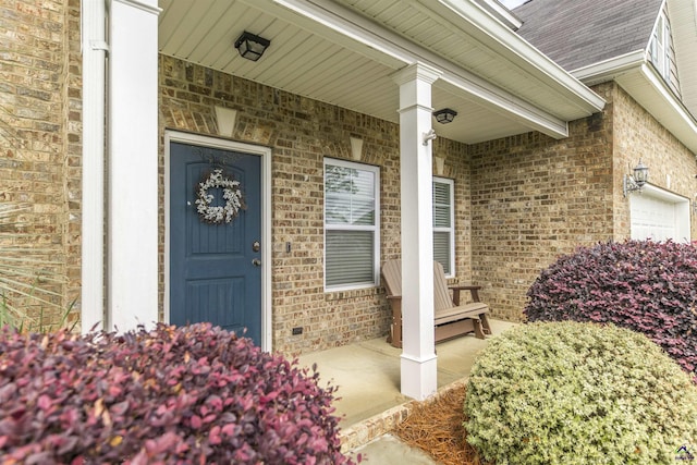 entrance to property featuring covered porch, brick siding, a shingled roof, and a garage
