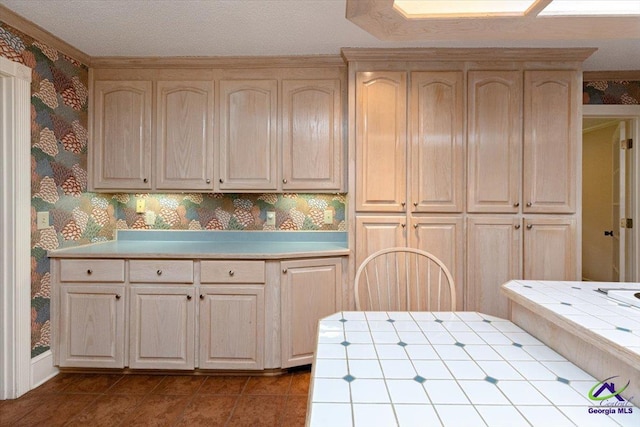 kitchen with tile countertops, wallpapered walls, light brown cabinets, and dark tile patterned flooring