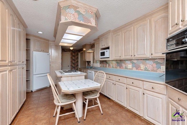 kitchen with white appliances, a textured ceiling, light tile patterned floors, light countertops, and wallpapered walls