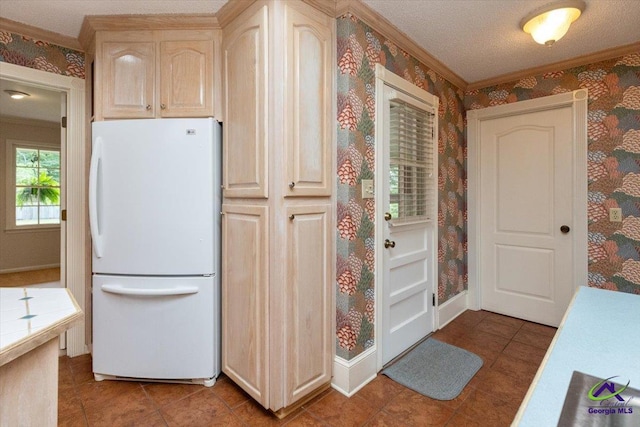 kitchen with freestanding refrigerator, wallpapered walls, tile counters, crown molding, and light tile patterned flooring