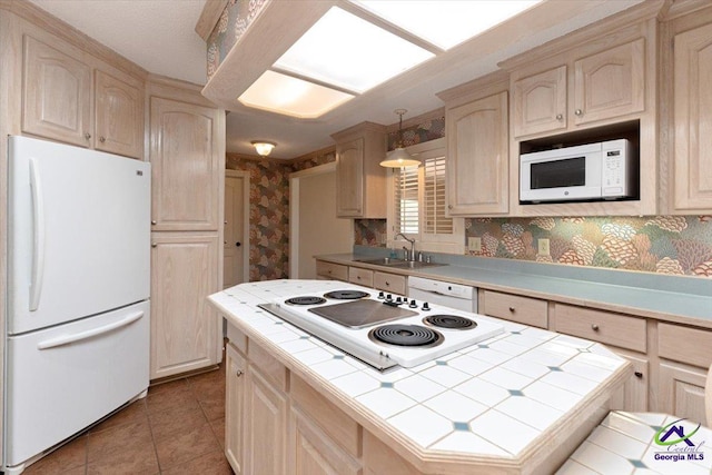 kitchen featuring white appliances, tile countertops, wallpapered walls, a sink, and a kitchen island