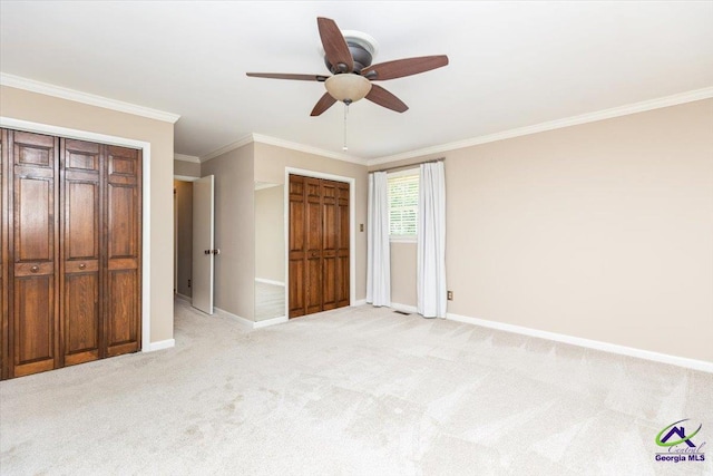 unfurnished bedroom with baseboards, crown molding, light carpet, ceiling fan, and two closets