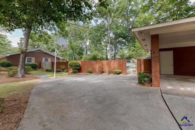 view of side of home with fence, a gate, brick siding, and driveway
