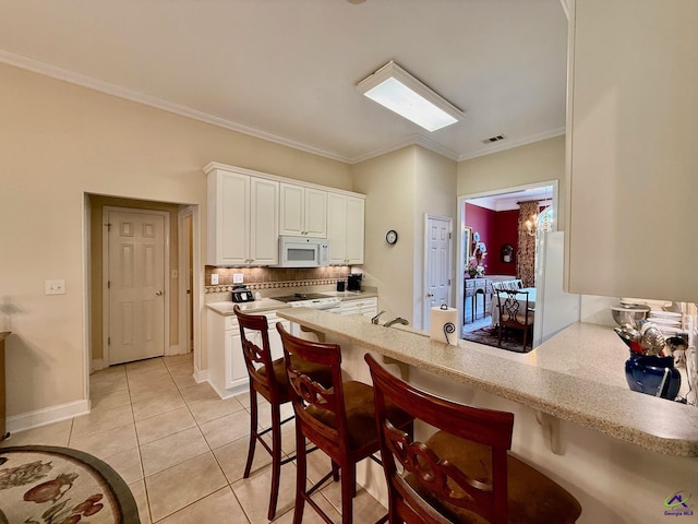 kitchen featuring white microwave, light tile patterned floors, decorative backsplash, a breakfast bar area, and white cabinets