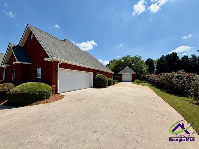 view of home's exterior featuring driveway, brick siding, roof with shingles, and an attached garage
